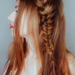 A woman with long red hair styled in a loose braid.